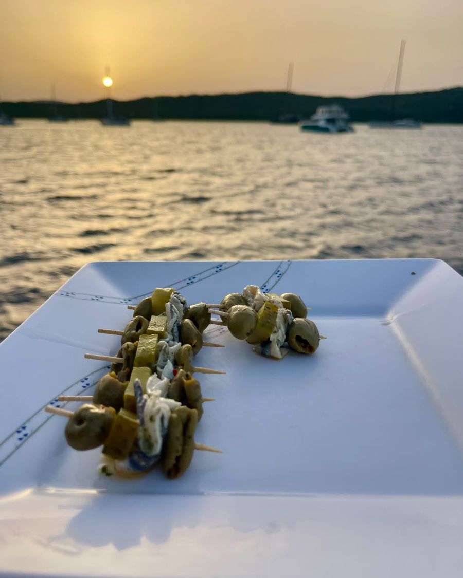 Brochetas de aceitunas al atardecer, con el barco fondeado en la bahía