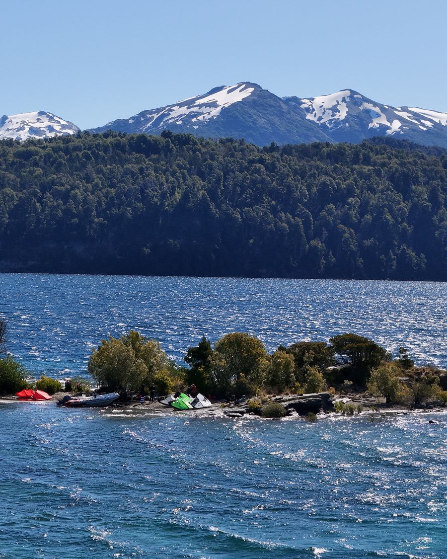 Isla con kites armados frente a cerros nevados, en un lago de Patagonia